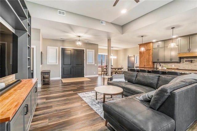 living area featuring a ceiling fan, visible vents, dark wood finished floors, and baseboards