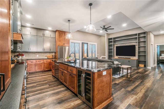 kitchen with stainless steel appliances, dark wood-style flooring, a sink, open floor plan, and dark stone countertops