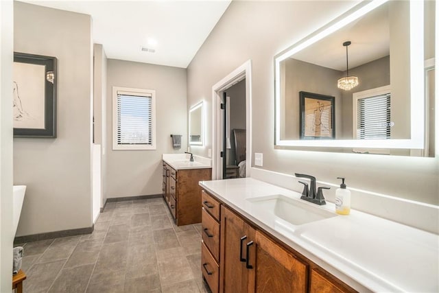 full bath with two vanities, visible vents, a sink, and baseboards