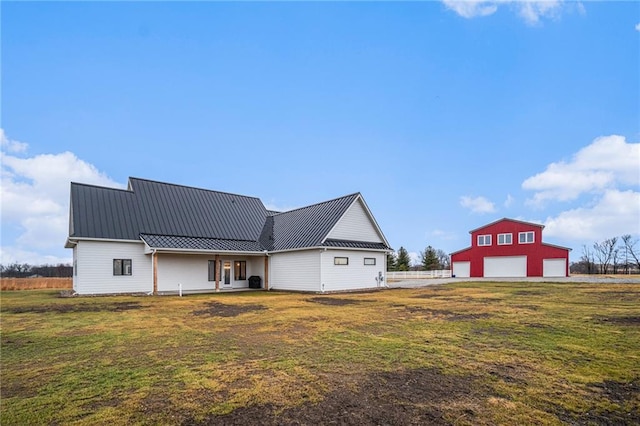 back of house featuring an outbuilding, metal roof, a yard, and a garage