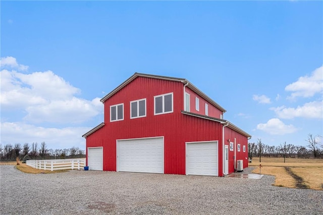 garage with central air condition unit, a detached garage, fence, and gravel driveway