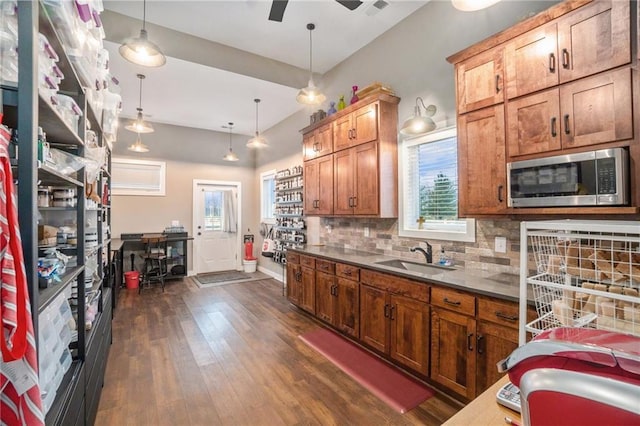 kitchen featuring dark wood-style flooring, a sink, hanging light fixtures, tasteful backsplash, and stainless steel microwave