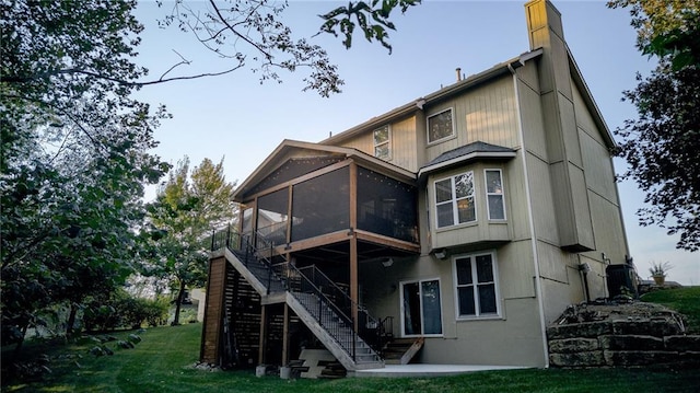 back of property with stairway, a lawn, a chimney, and a sunroom