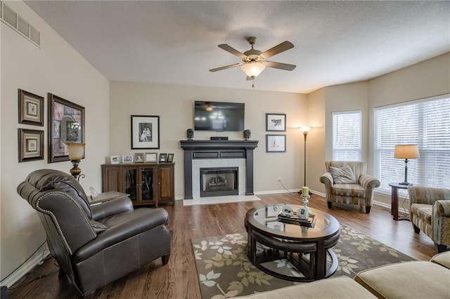 living room featuring visible vents, a fireplace with flush hearth, ceiling fan, and wood finished floors