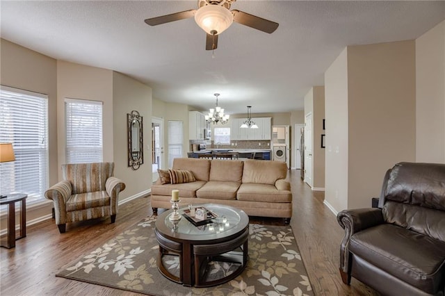 living area with dark wood finished floors, washer / dryer, ceiling fan with notable chandelier, and baseboards