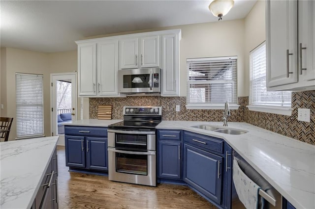 kitchen with light wood finished floors, blue cabinetry, a sink, white cabinets, and appliances with stainless steel finishes