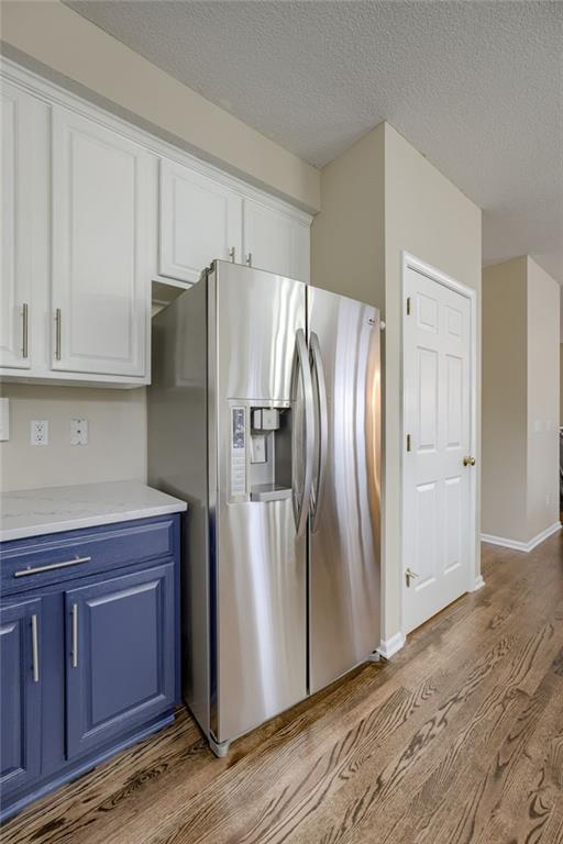 kitchen featuring blue cabinetry, light countertops, stainless steel refrigerator with ice dispenser, wood finished floors, and white cabinets