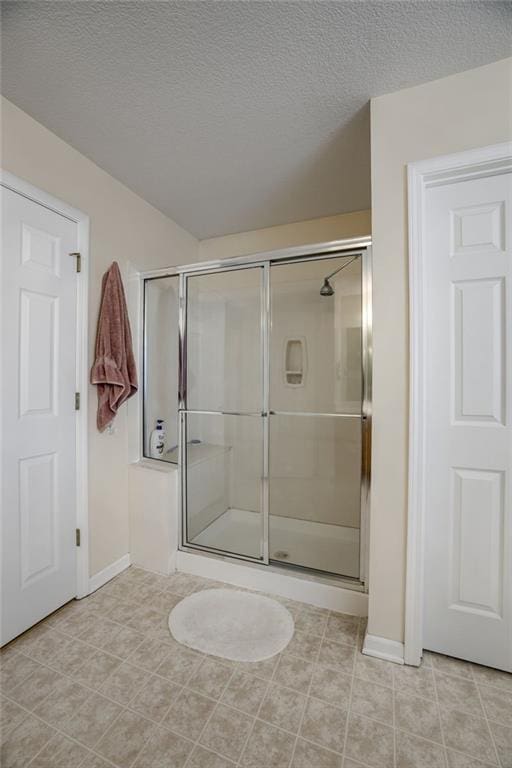 full bathroom featuring baseboards, a textured ceiling, a stall shower, and tile patterned flooring