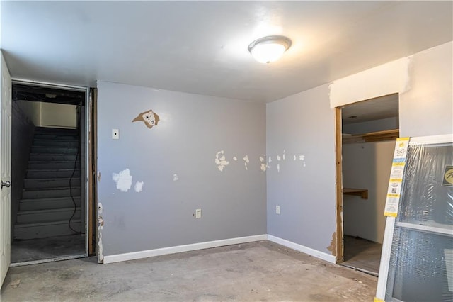 spare room featuring stairs, unfinished concrete flooring, and baseboards