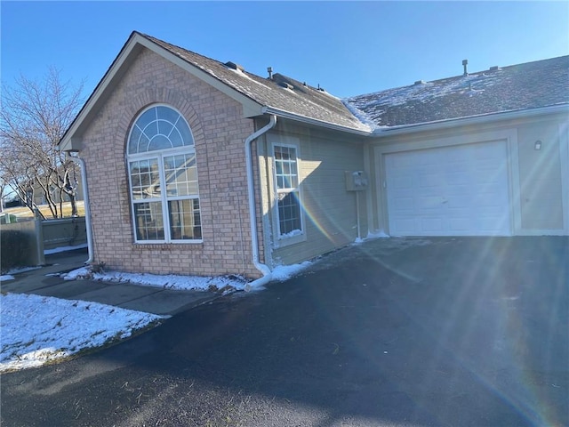 view of property exterior featuring a garage, a shingled roof, aphalt driveway, and brick siding