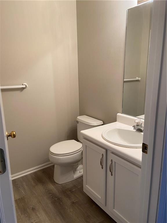 half bathroom with vanity, wood finished floors, toilet, and baseboards