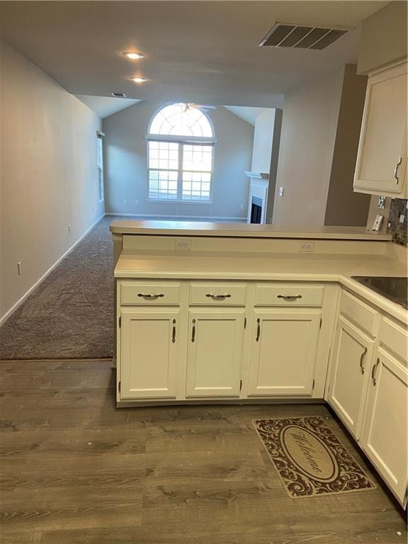 kitchen with vaulted ceiling, a peninsula, visible vents, and white cabinetry