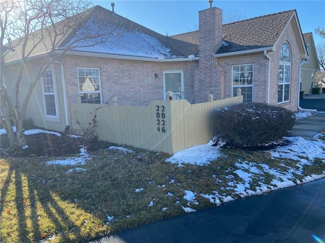 view of snowy exterior with a chimney, fence, and brick siding