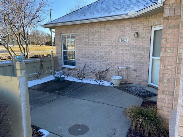 view of property exterior with roof with shingles, fence, a patio, and brick siding