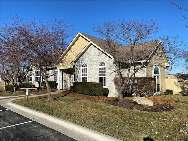 view of front of property featuring uncovered parking, stone siding, roof with shingles, and a front yard