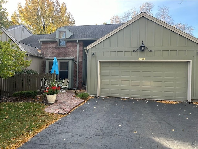 view of front of home with brick siding, board and batten siding, fence, driveway, and an attached garage