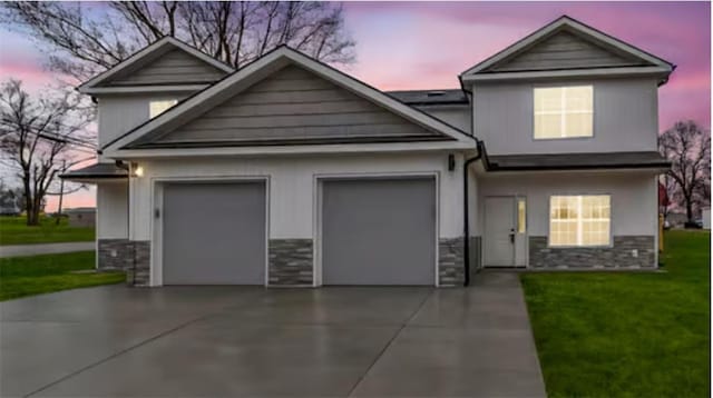 view of front of house featuring an attached garage, stone siding, concrete driveway, and a front yard