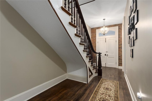 foyer with baseboards, dark wood finished floors, brick wall, stairs, and a chandelier