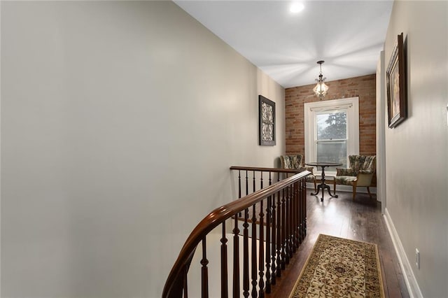 corridor with brick wall, baseboards, wood finished floors, and an upstairs landing