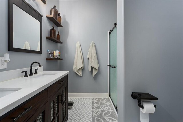 bathroom with a stall shower, a sink, baseboards, and double vanity