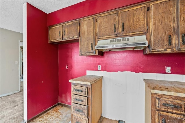 kitchen with a textured ceiling, light countertops, baseboards, and under cabinet range hood