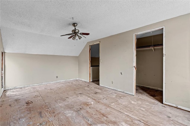 unfurnished bedroom with lofted ceiling, a textured ceiling, a ceiling fan, a closet, and a walk in closet