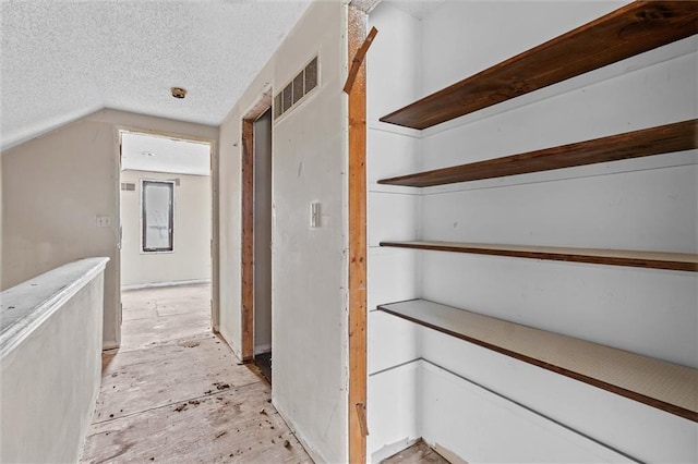 hall featuring a textured ceiling, lofted ceiling, and visible vents