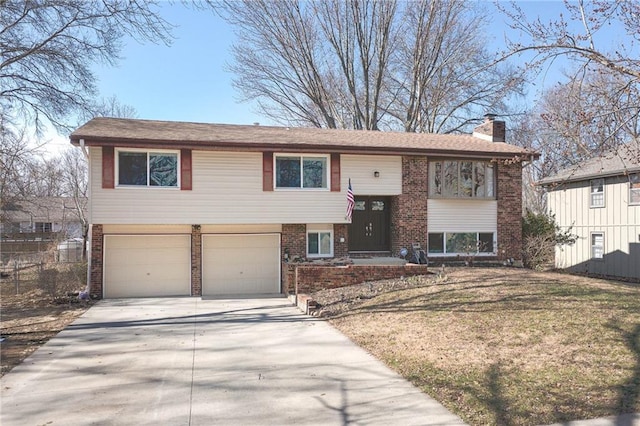 raised ranch with brick siding, a chimney, concrete driveway, an attached garage, and fence