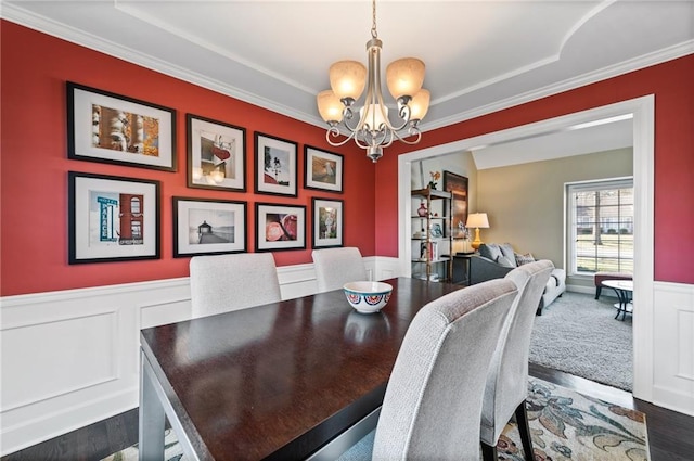 dining space featuring a chandelier, a wainscoted wall, dark wood finished floors, and ornamental molding