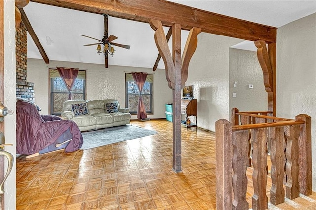 living area with vaulted ceiling with beams, a ceiling fan, and a textured wall