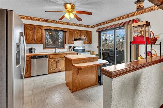 kitchen featuring brown cabinets, light countertops, appliances with stainless steel finishes, a sink, and under cabinet range hood