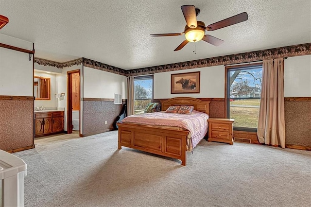 bedroom featuring light colored carpet, visible vents, wainscoting, a textured ceiling, and ensuite bath