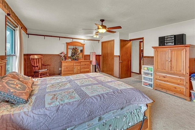 carpeted bedroom with a wainscoted wall, a textured ceiling, a ceiling fan, and wooden walls