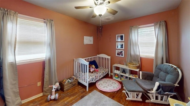 bedroom featuring visible vents, ceiling fan, wood finished floors, and a nursery area
