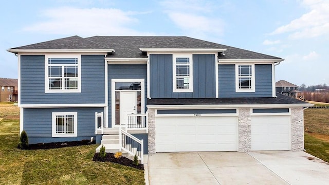 raised ranch featuring driveway, stone siding, an attached garage, a front lawn, and board and batten siding