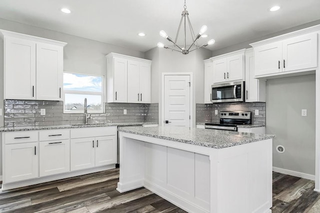 kitchen with dark wood-style floors, appliances with stainless steel finishes, white cabinets, a kitchen island, and a sink