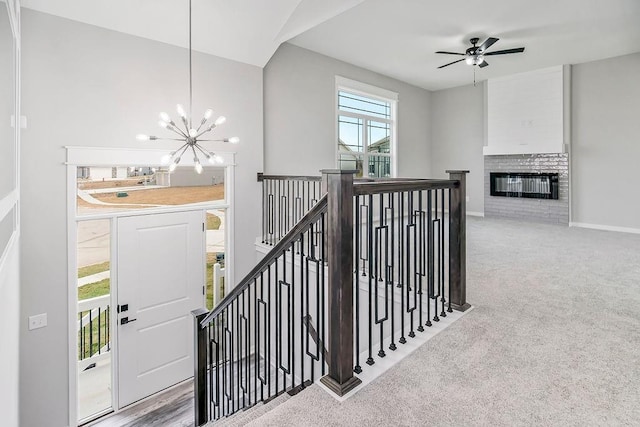 staircase featuring ceiling fan with notable chandelier, carpet floors, a brick fireplace, and baseboards