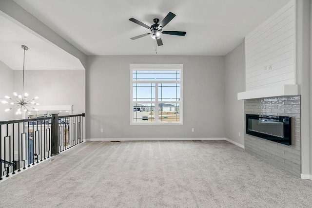 unfurnished living room featuring a brick fireplace, carpet flooring, baseboards, and ceiling fan with notable chandelier