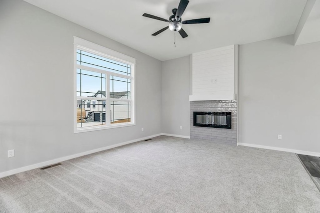 unfurnished living room with carpet floors, a ceiling fan, visible vents, baseboards, and a brick fireplace