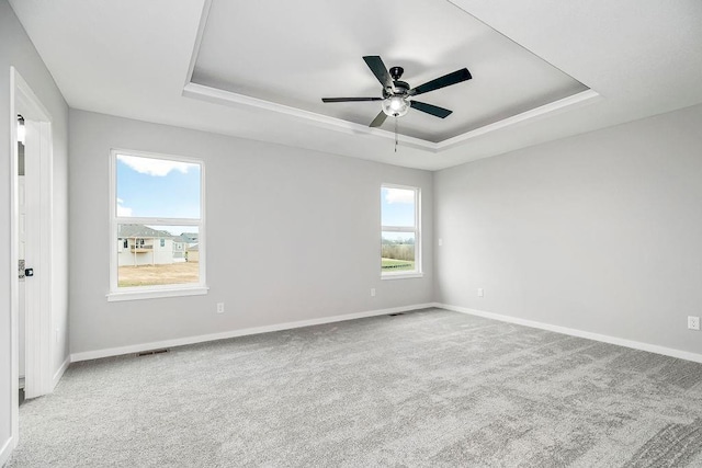 carpeted spare room featuring baseboards, visible vents, a tray ceiling, and ceiling fan