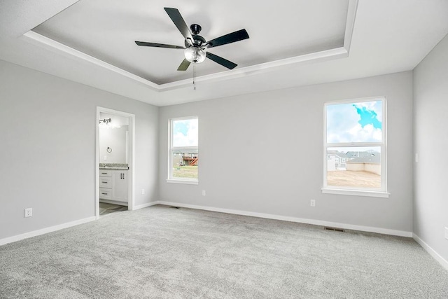 unfurnished bedroom with carpet floors, a ceiling fan, baseboards, a raised ceiling, and ensuite bath