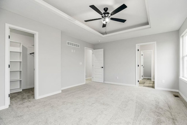 unfurnished bedroom with baseboards, visible vents, a raised ceiling, a walk in closet, and carpet floors