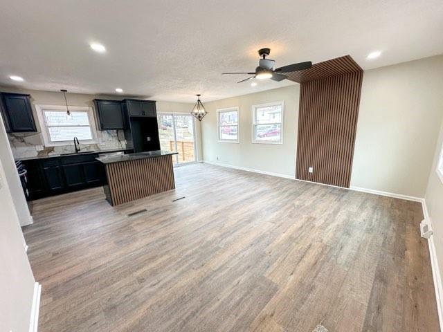 kitchen with light wood finished floors, baseboards, open floor plan, a center island, and a sink