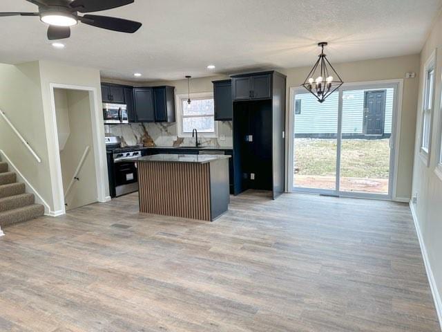 kitchen featuring a sink, a center island, light wood-style floors, appliances with stainless steel finishes, and decorative backsplash