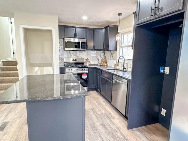 kitchen featuring light wood-style floors, dark stone countertops, appliances with stainless steel finishes, and a sink