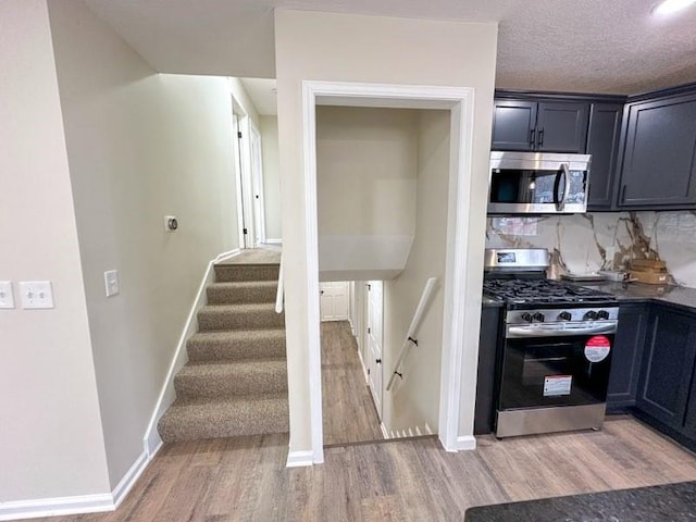 kitchen with baseboards, decorative backsplash, light wood-style flooring, appliances with stainless steel finishes, and a textured ceiling