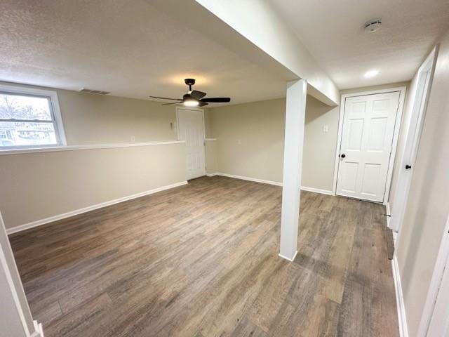 basement featuring a textured ceiling, wood finished floors, a ceiling fan, and baseboards