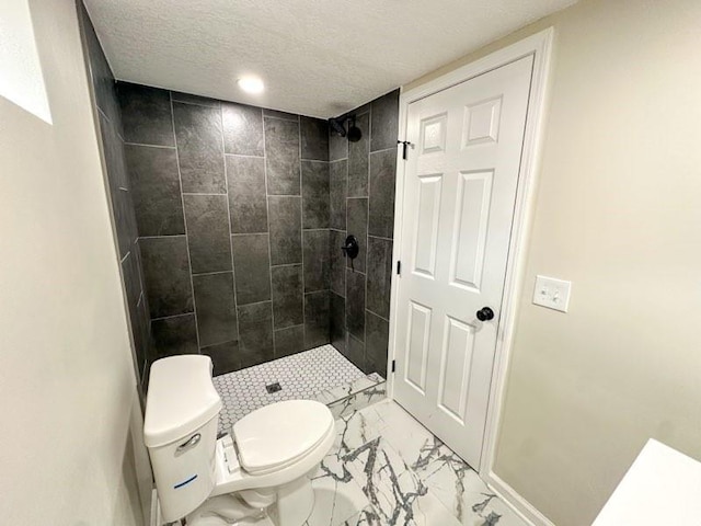 bathroom featuring a textured ceiling, marble finish floor, a tile shower, and toilet