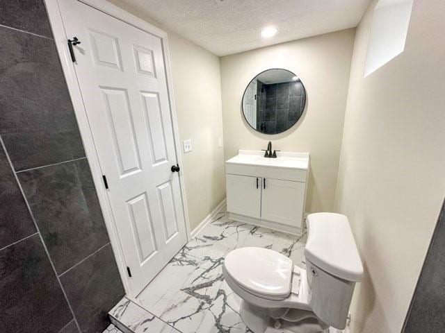 bathroom with a textured ceiling, toilet, vanity, baseboards, and marble finish floor