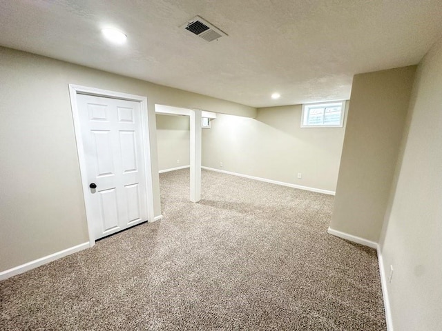 basement featuring a textured ceiling, recessed lighting, visible vents, baseboards, and carpet